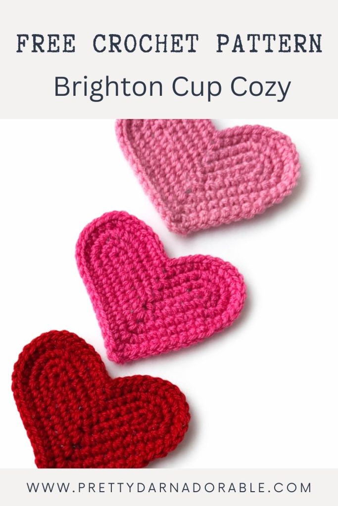 Three red, pink, and dark pink crocheted hearts on white with text: Free Crochet Pattern: Brighton Cup Cozy; link for crochet guide. Free crochet pattern