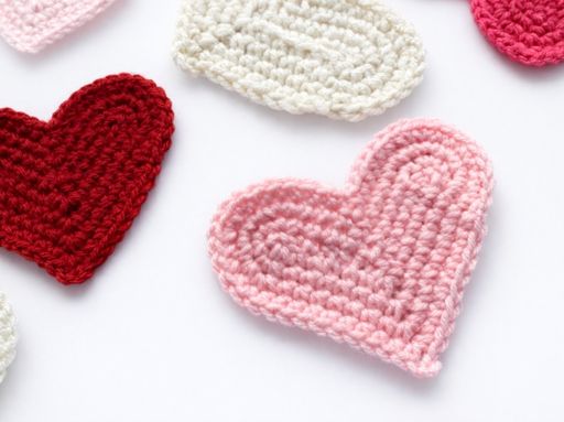 Pink, red, and white crocheted hearts are arranged on a white background with "HOW TO CROCHET A HEART" in bold text. Free crochet pattern