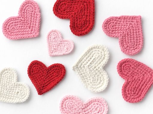 Red, pink, and white crocheted hearts with textured stitching are scattered on a white background, inspiring how to crochet a heart. Free crochet pattern