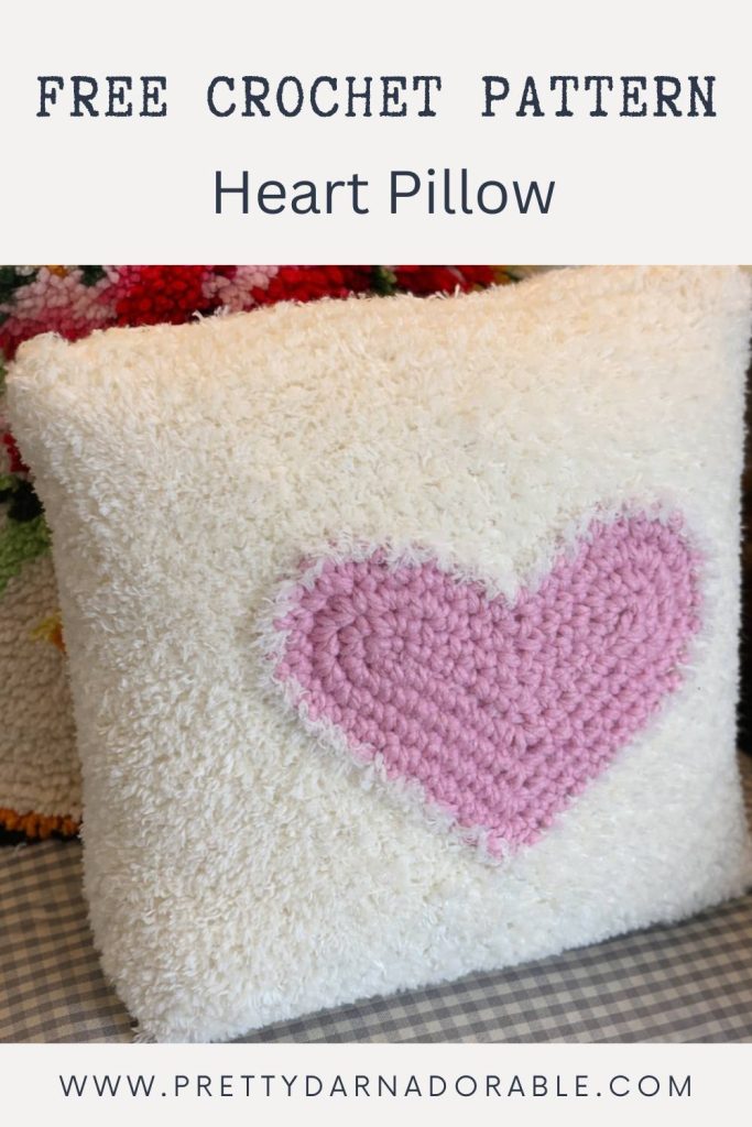 A soft white crochet pillow with a pink heart in the center. Text reads Free Crochet Heart Pillow Pattern and www.prettydarnadorable.com. Free crochet pattern
