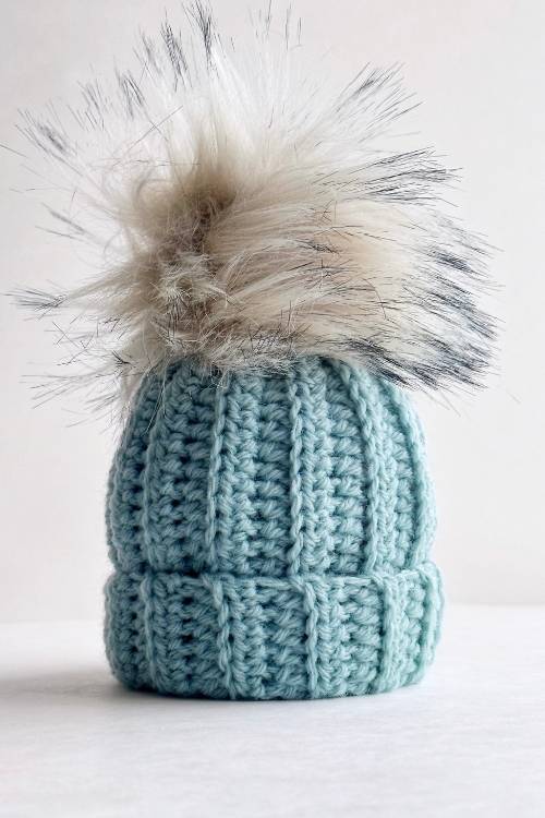 Light blue ribbed beanie with a white and gray faux fur pom-pom on top, shown against a plain white background. Free crochet pattern