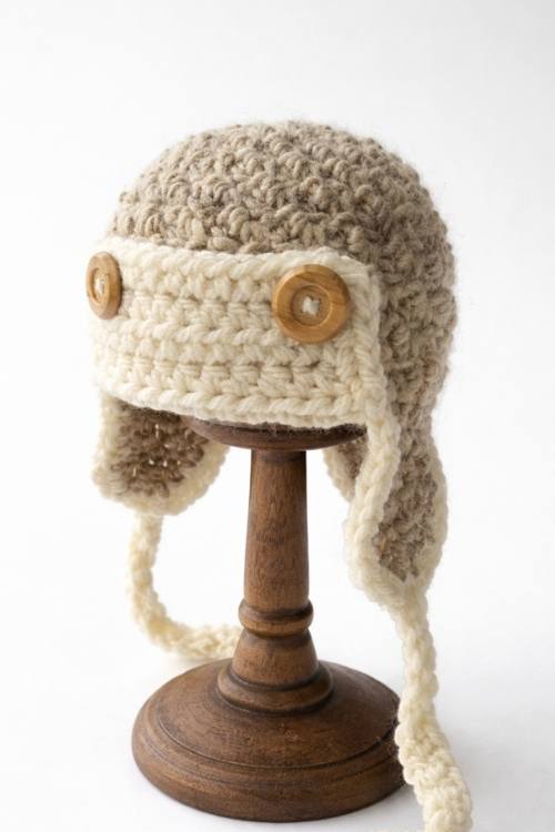 Adult-sized crochet aviator hat with ear flaps and two wooden buttons on a wooden stand, set against a white background. Free crochet pattern