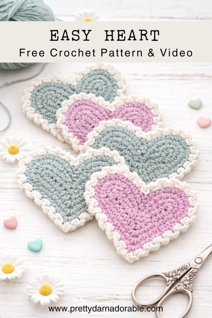 Four crocheted hearts—two pink, two light blue with white edges—lie on white wood with daisies, pastel beads, scissors, and yarn. Free crochet pattern