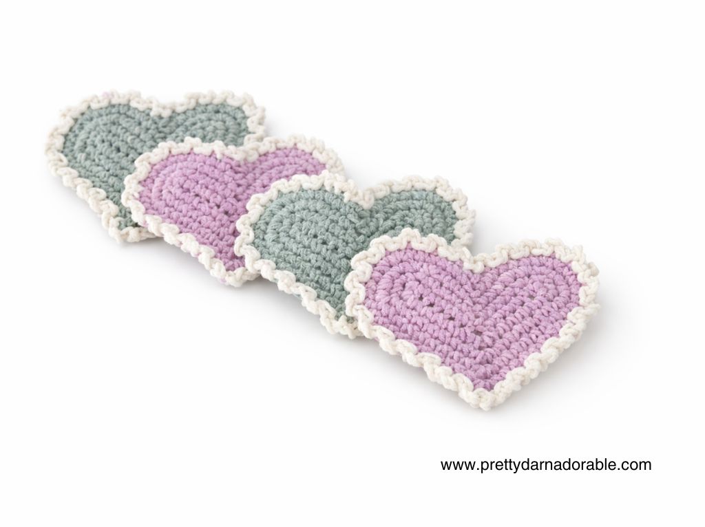 Four crocheted hearts, two pink and two green with white ruffled edges, lined up on white. Free pattern at prettydarnadorable.com. Free crochet pattern