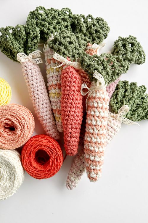 Pastel crocheted carrots with green tops beside yellow, white, red, and orange yarn on a white surface; "Free Crochet Carrot Pattern" shown. Free crochet pattern