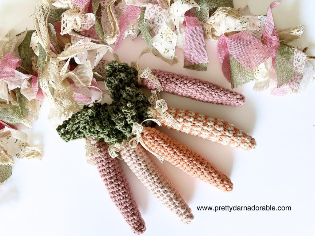 group of crochet carrots with green tops in solid and stripes with easter garland