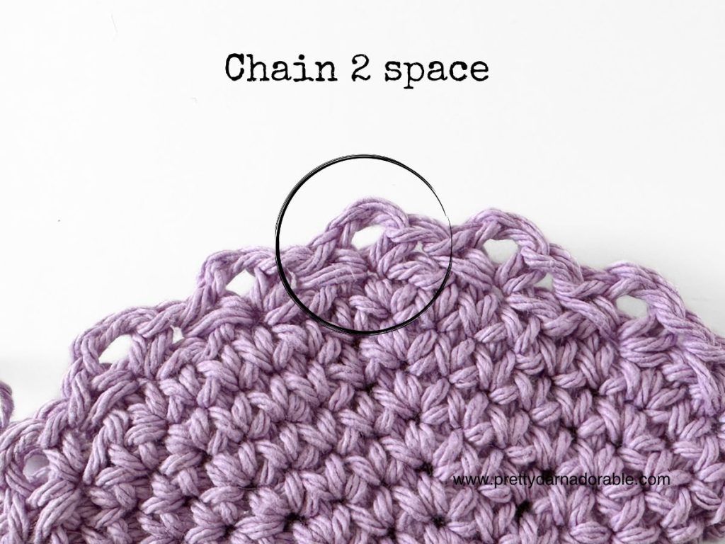 A close-up of a purple crocheted piece with a circle highlighting the &ldquo;chain 2 space.&rdquo; The words &ldquo;Chain 2 space&rdquo; are written above, referencing a free crochet bucket hat pattern. The website www.prettyandadorable.com appears at the bottom right.