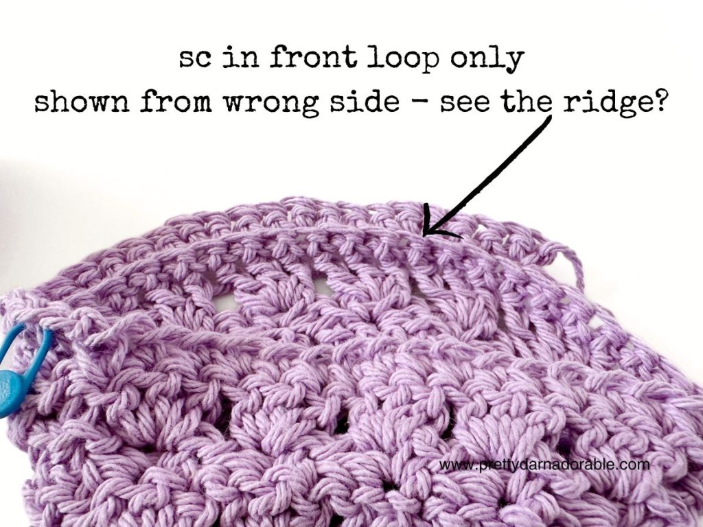 A close-up of a lavender crochet piece with text pointing to a row, explaining &ldquo;sc in front loop only shown from wrong side&mdash;see the ridge?&rdquo; A blue stitch marker is attached to the edge, perfect for your next free crochet bucket hat pattern.