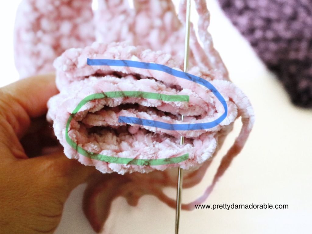 a person is holding a pink crocheted piece of fabric with a needles sewing together