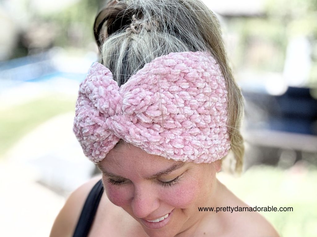 a woman wearing a pink crochet headband with a twist made out of velvet yarn