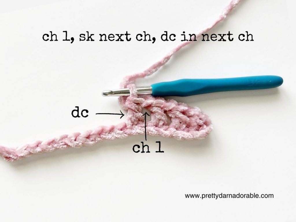 a crocheted piece of pink yarn with a blue crochet hook