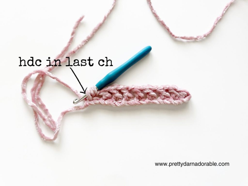 a crocheted piece of pink yarn with a blue crochet hook
