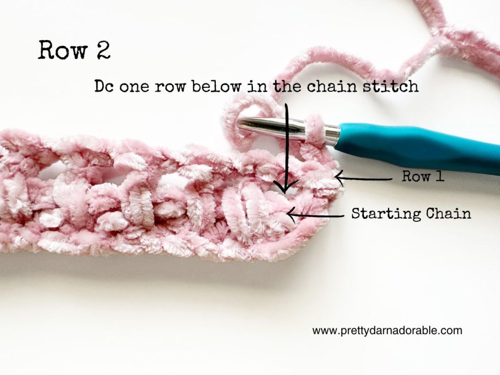 a crocheted piece of pink yarn with a blue crochet hook