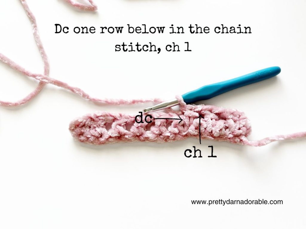 a crocheted piece of pink yarn with a blue crochet hook