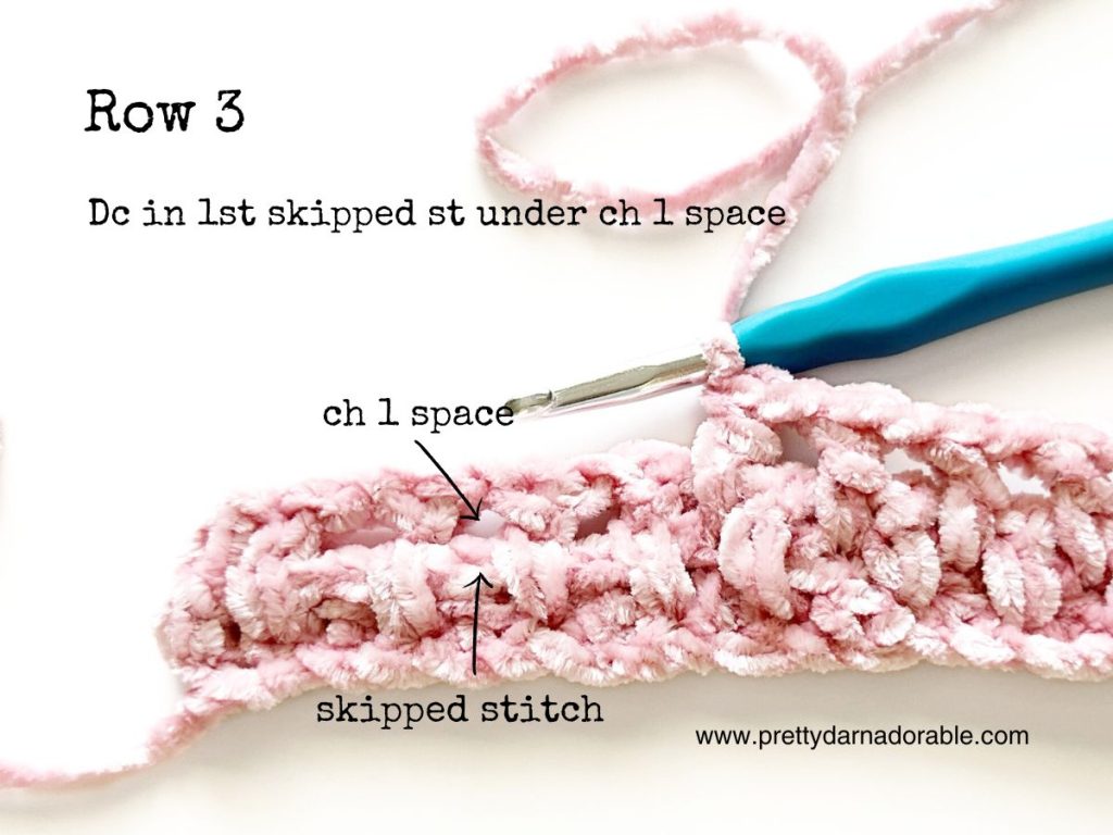 a crocheted piece of pink yarn with a blue crochet hook