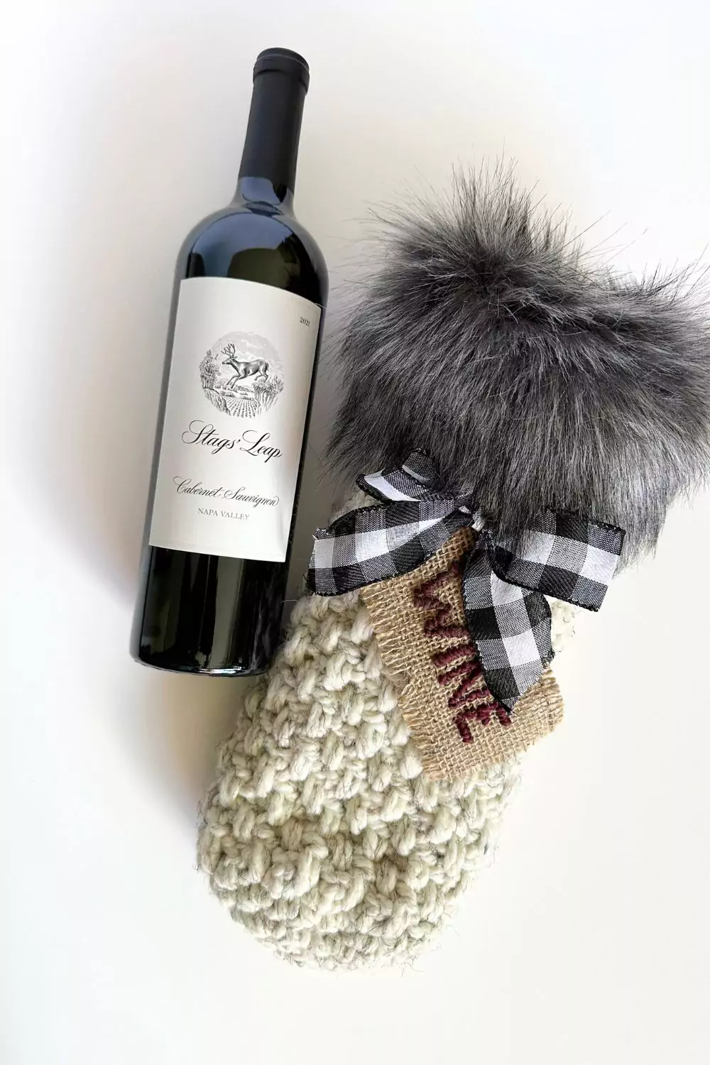 a bottle of wine and a crocheted wine bottle gift bag with faux fur fabric trim, checkered bow and wine tag