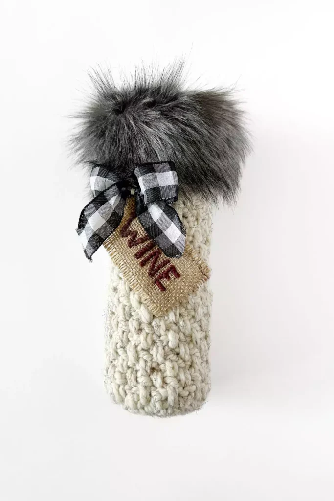 a bottle of wine and a crocheted wine bottle gift bag with faux fur fabric trim, checkered bow and wine tag