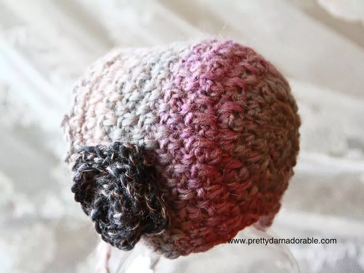 a crochet baby bonnet with a rose in pink and purple back view