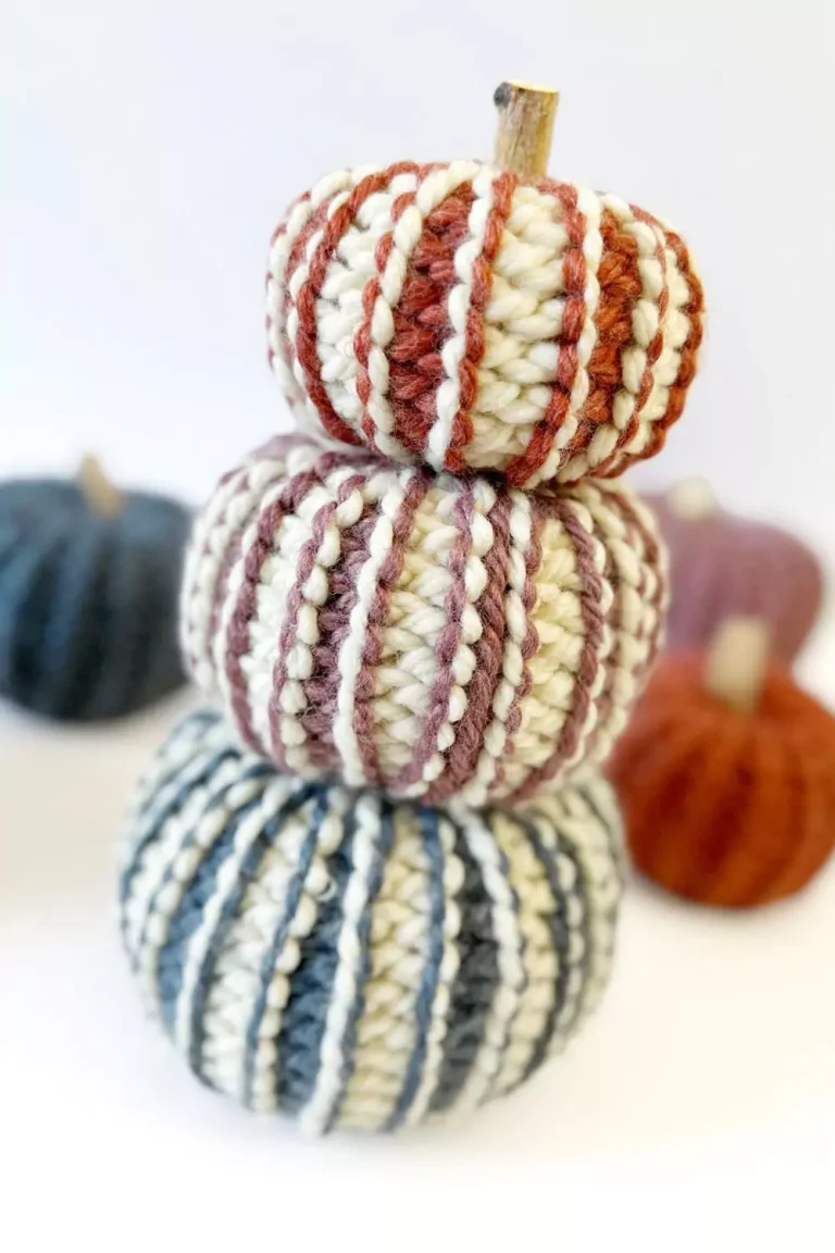 Three striped, yarn-wrapped pumpkins stacked on a white surface; two more blurred in the background, no visible text. Free crochet pattern