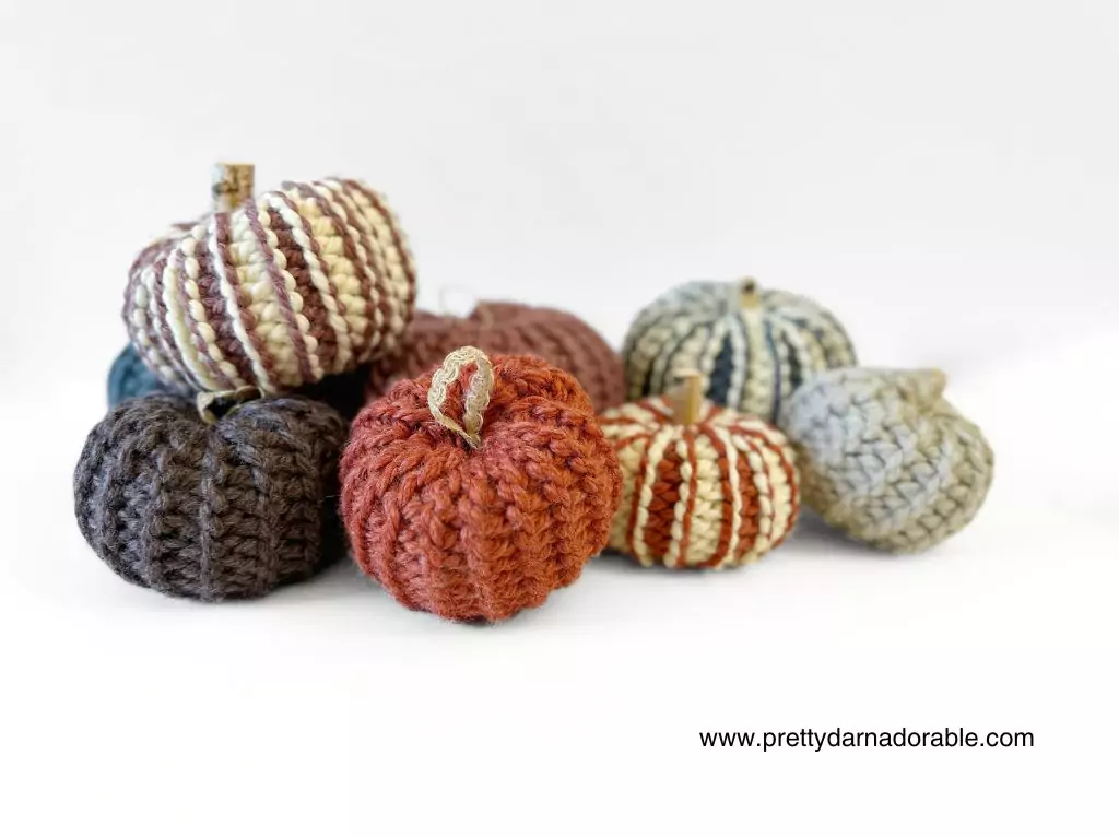 Chunky crocheted pumpkins in orange, brown, cream, gray, and blue grouped on white; pumpkin pattern URL shown at lower right. Free crochet pattern