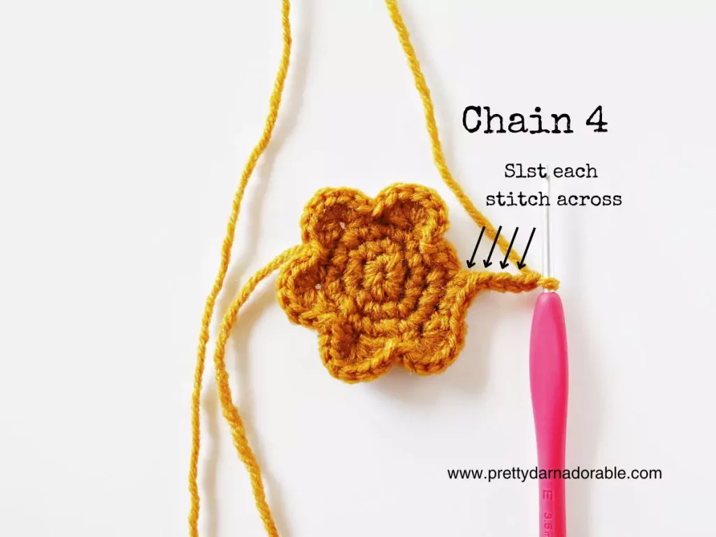Yellow crocheted flower with pink hook in a stitch, text: &ldquo;Chain 4, Slst each stitch across,&rdquo; arrows highlight stitches; site at bottom. Free crochet pattern