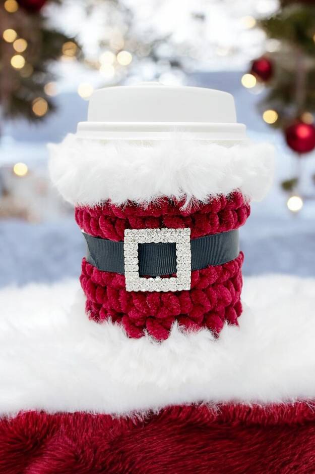 red crochet cup cozy with fur trim rhinestone buckle and black belt - looks like santa with christmas theme in the background
