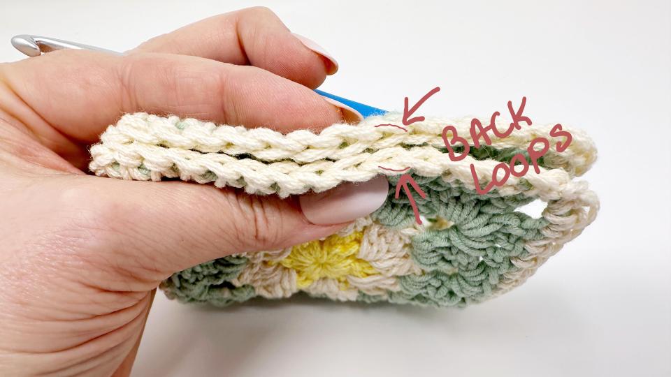 A hand holds a crochet project, showing a close-up of the stitches. An arrow highlights the BACK LOOPS of the top row—perfect for those working on granny square placemat free patterns and learning where to insert the hook.