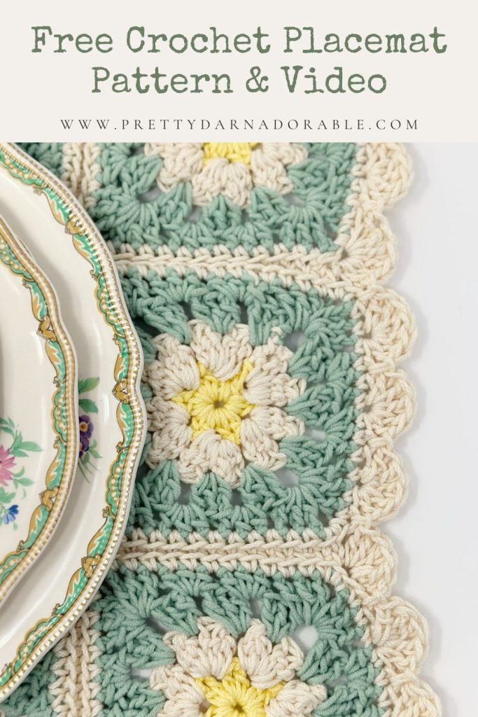 A close-up of a green, cream, and yellow crochet placemat with a scalloped edge, perfect for kitchen decor, sits beside floral plates. Text above reads, “Free Crochet Placemat Pattern & Video Tutorial.”.