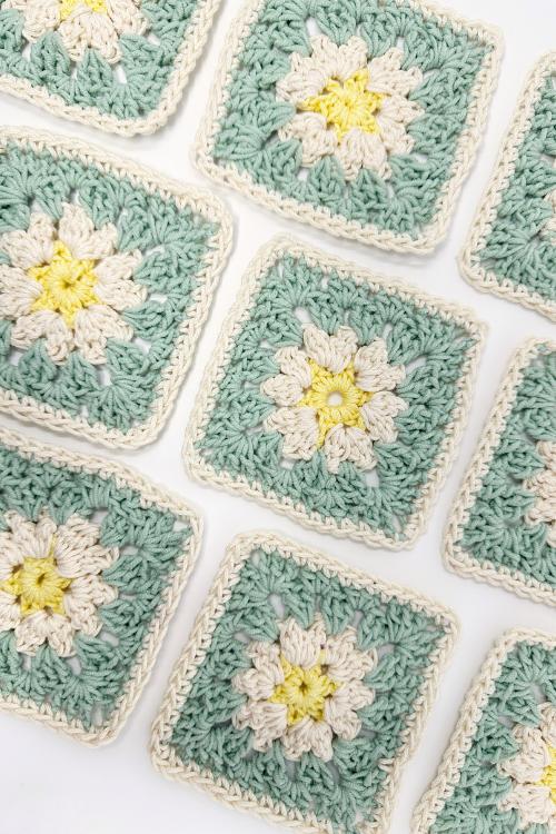 Crocheted granny squares with a white and yellow flower pattern in the center, surrounded by pale green and finished with a cream border—perfect inspiration if you’re searching for granny square placemat free patterns. Arranged in a neat grid on a white background.