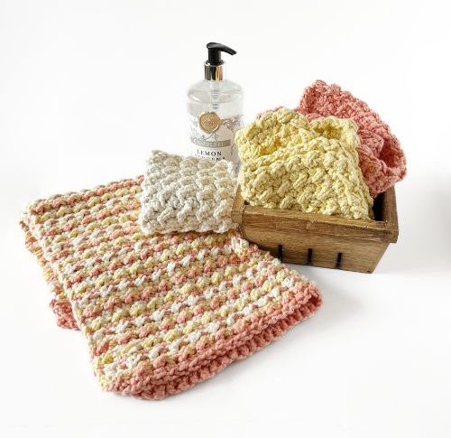 oft, crocheted washcloths in pastel shades of white, peach, and yellow are layered against a bright background, conveying warmth and coziness.