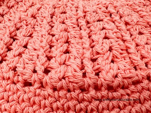 Close-up of a crocheted fabric in pink yarn, showing textured, chunky stitches and a repeating pattern&mdash;perfect inspiration for anyone seeking a free crochet bucket hat pattern. The material appears soft and thick.