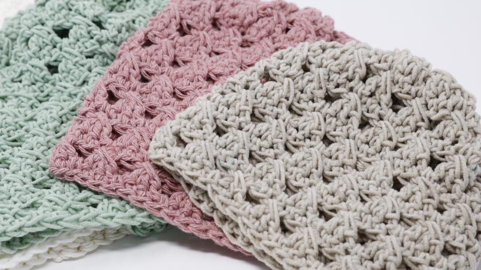 Three crocheted beanies in pastel hues—sage green, dusty pink, and light beige—overlap on a white surface, their textured patterns reminiscent of a simple granny stitch crochet beanie.