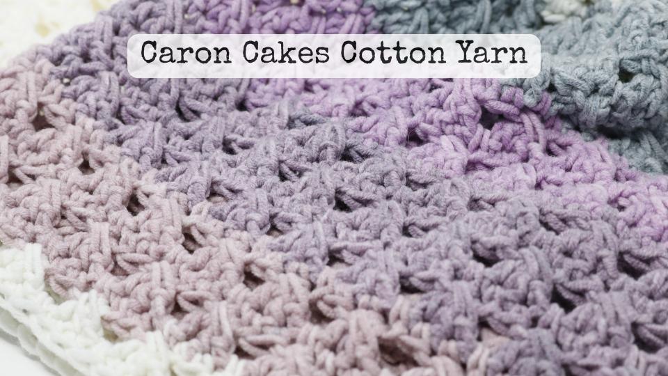Close-up of a crocheted fabric in gradient shades of white, lavender, purple, and gray, perfect for making a simple granny stitch crochet beanie. The text Caron Cakes Cotton Yarn is overlaid near the top.