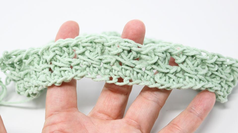 A hand holds a piece of light green crocheted fabric with an open, lacy crochet granny stitch pattern against a plain white background—perfect inspiration for your next free crochet pattern.