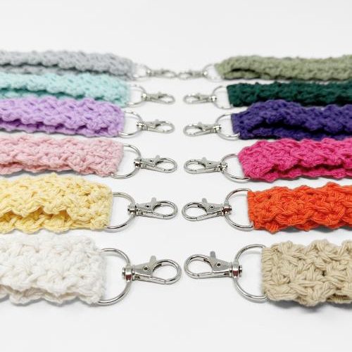Nine crocheted keychains in various colors, each with a silver clasp, are arranged in parallel rows on a white background. Discover inspiration for your own creations with these vibrant crochet keychain patterns free to try.