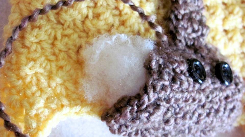 Close-up of yellow crocheted fabric with a brown bear shape, black button eyes, and white stuffing exposed from a hole. Free crochet pattern
