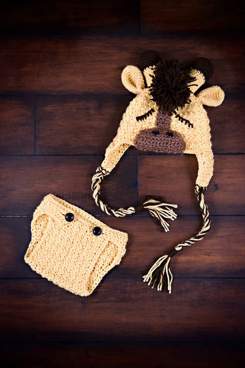 Yellow crocheted baby giraffe hat with ears and horns, plus matching diaper cover with two dark buttons on a wooden surface. Free crochet pattern