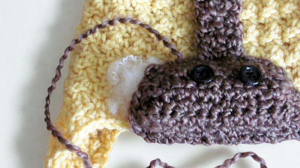 Close-up of a yellow and brown crocheted stuffed animal with black button eyes and white stuffing visible from a tear. Free crochet pattern
