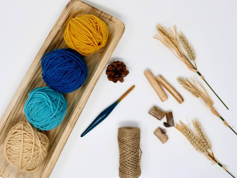 Yellow, blue, teal, and beige yarn balls in a wooden tray with a crochet hook; pine cone, twine, and cinnamon sticks nearby. Free crochet pattern