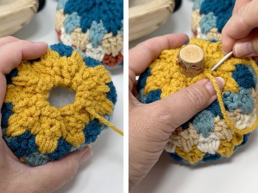 Hands crochet a striped blue, yellow, and beige cover on a round object; a hook secures yellow yarn around a central cork.