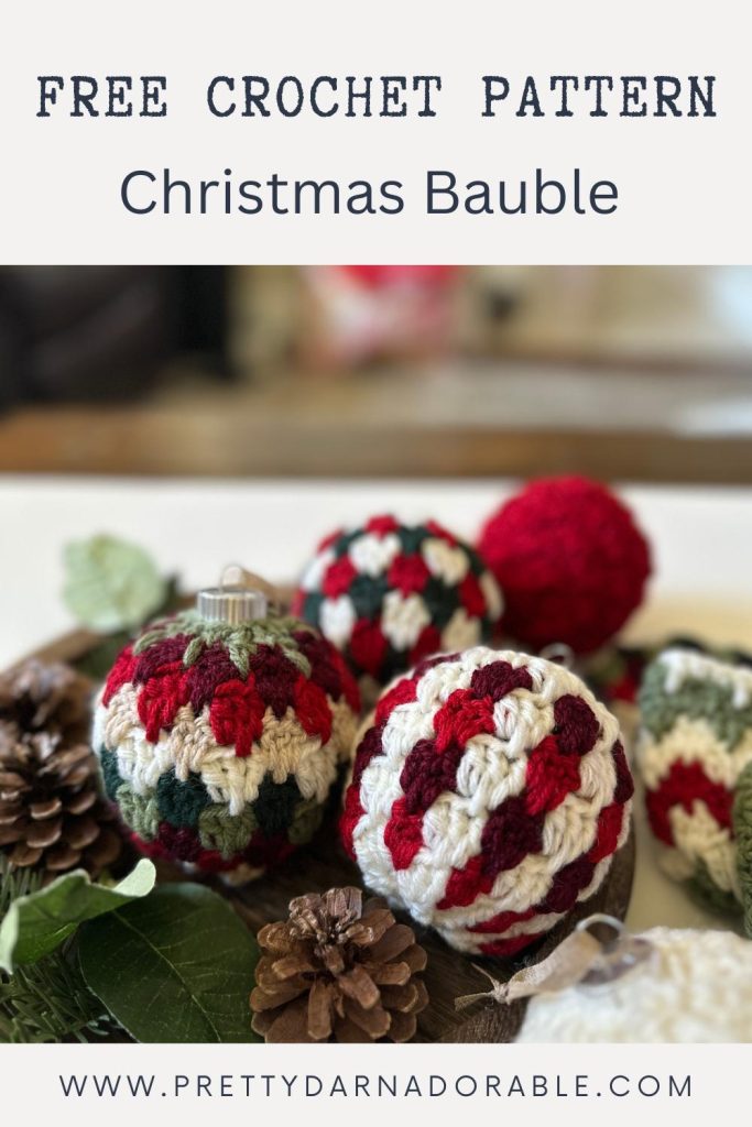 Colorful crocheted Christmas baubles in red, green, and white sit with pinecones; text reads Free Crochet Pattern Christmas Bauble. Free crochet pattern