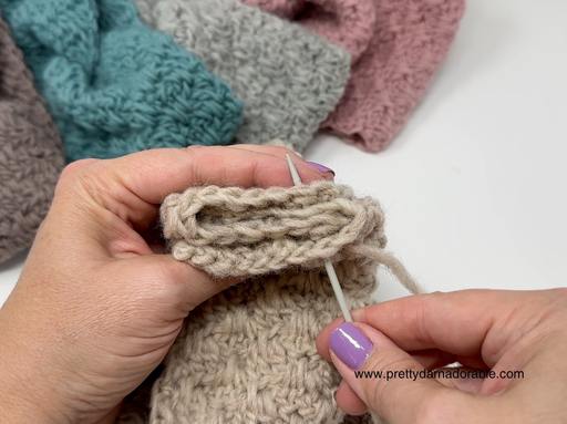 Hands with purple nail polish use a yarn needle to sew beige fabric; gray, teal, and pink yarn crafts are in the background. Free crochet pattern