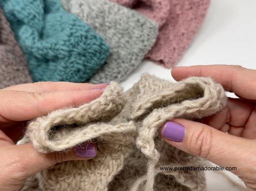 Close-up of hands with purple nail polish joining two edges of beige textured fabric; teal, pink, and gray fabrics in background. Free crochet pattern