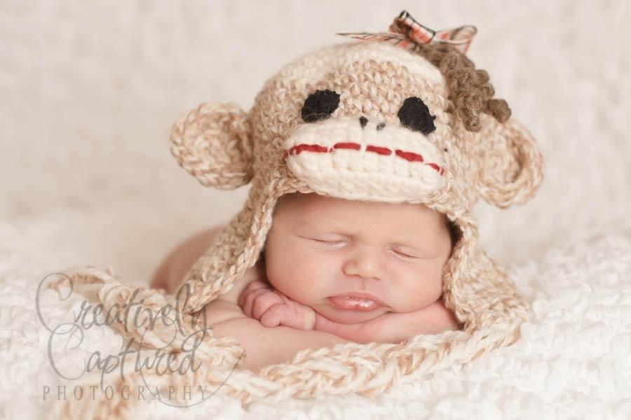A baby sleeps on a white surface, wearing a beige monkey hat with ears and face details, arms folded under their head. Free crochet pattern