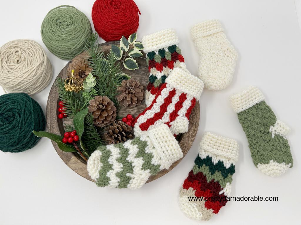 A wooden tray holds pinecones, faux greenery, and red berries, with yarn balls and five small crocheted stockings in holiday colors. Free crochet pattern
