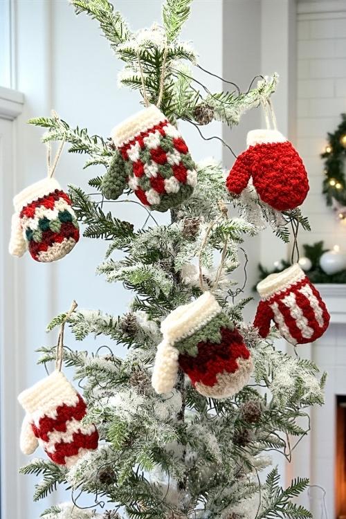 A snow-dusted Christmas tree with colorful red, white, and green mitten ornaments stands in a bright, festive room. Free crochet pattern