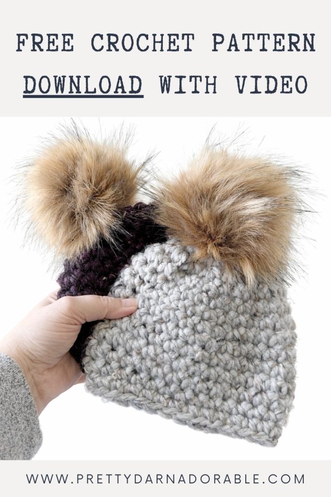 Hand holding a grey and dark purple chunky crocheted hat with two faux fur pom-poms; text offers free pattern at prettydarnadorable.com. Free crochet pattern