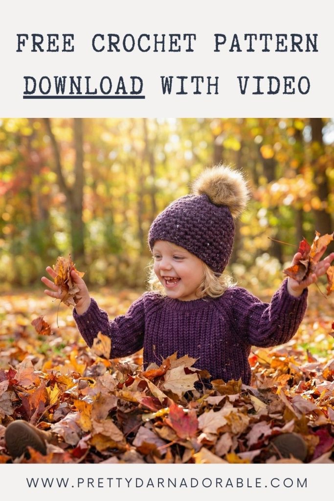 Smiling child in a purple sweater and pom-pom hat sits in autumn leaves, holding them up. Text advertises free crochet pattern and video; website URL below. Free crochet pattern
