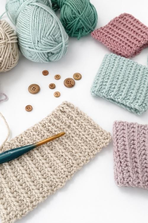 Pastel yarn balls, crocheted swatches, a crochet hook, and wooden buttons are laid out on a white background. Free crochet pattern