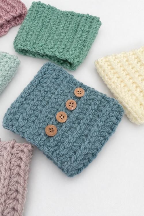Pastel crocheted square swatches, one blue with four brown buttons, are arranged on a white surface. No visible text. Free crochet pattern
